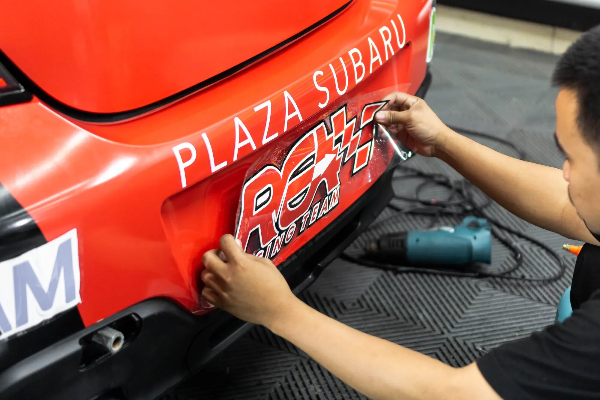 Teknisi memasang livery wrapping Plaza Subaru di bumper belakang